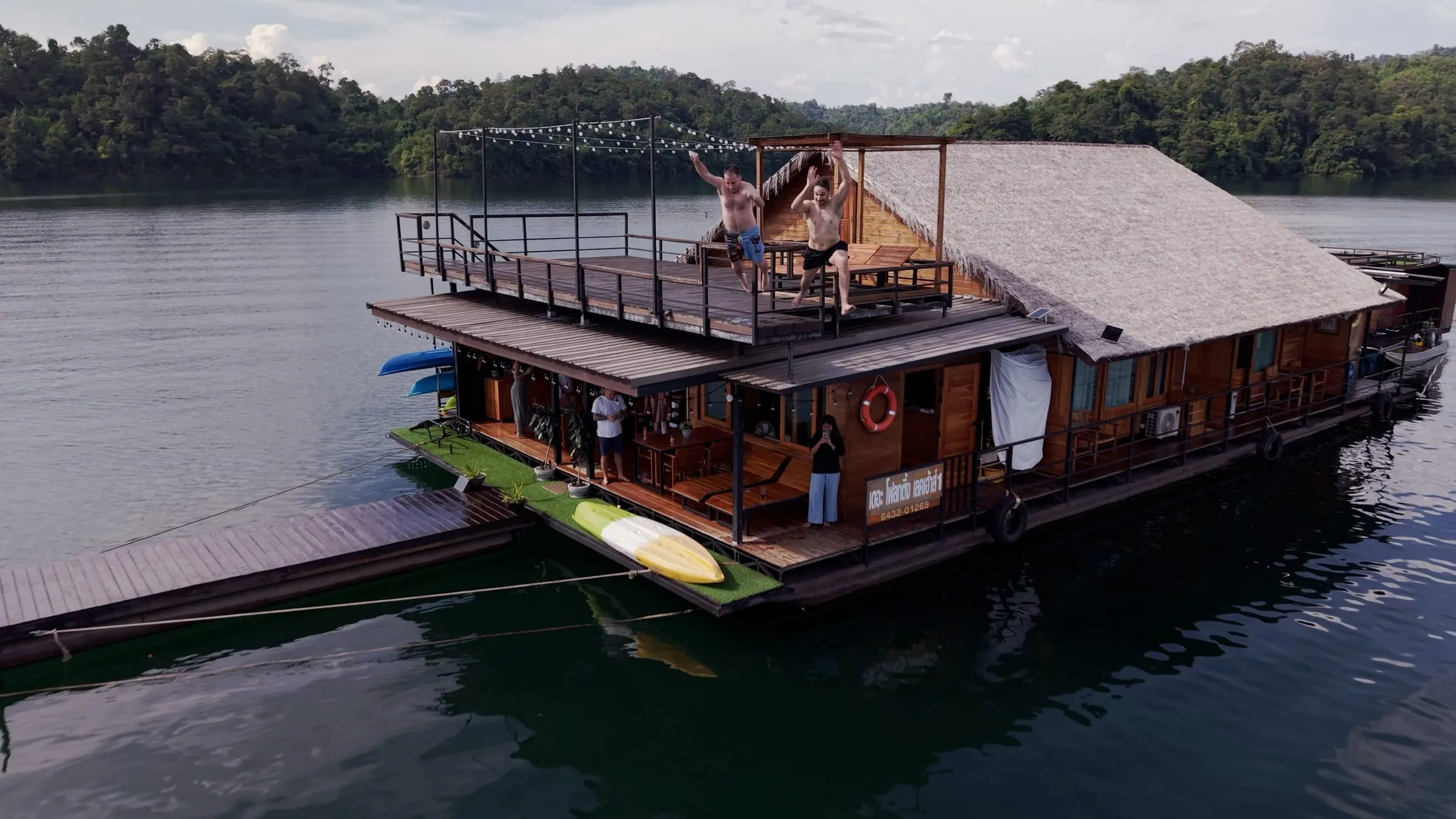 Aerial view of the wooden floating lake house with people relaxing on its upper deck.
