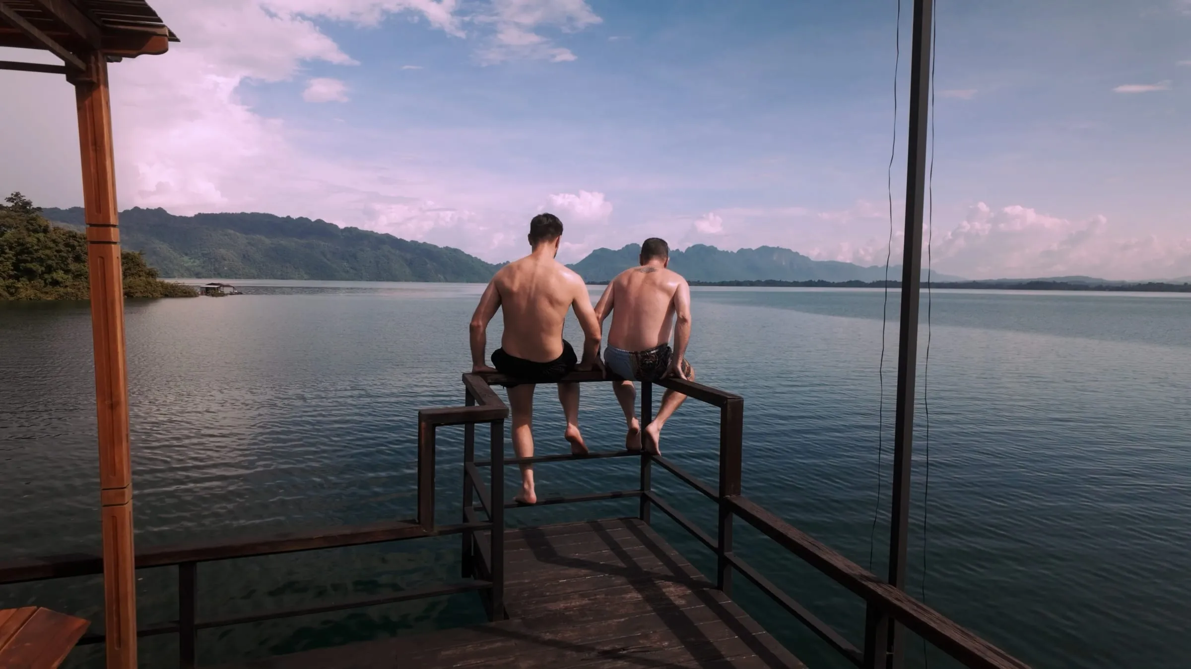 A couple sitting on the deck of the floating house watching a pastel sunset over the lake.