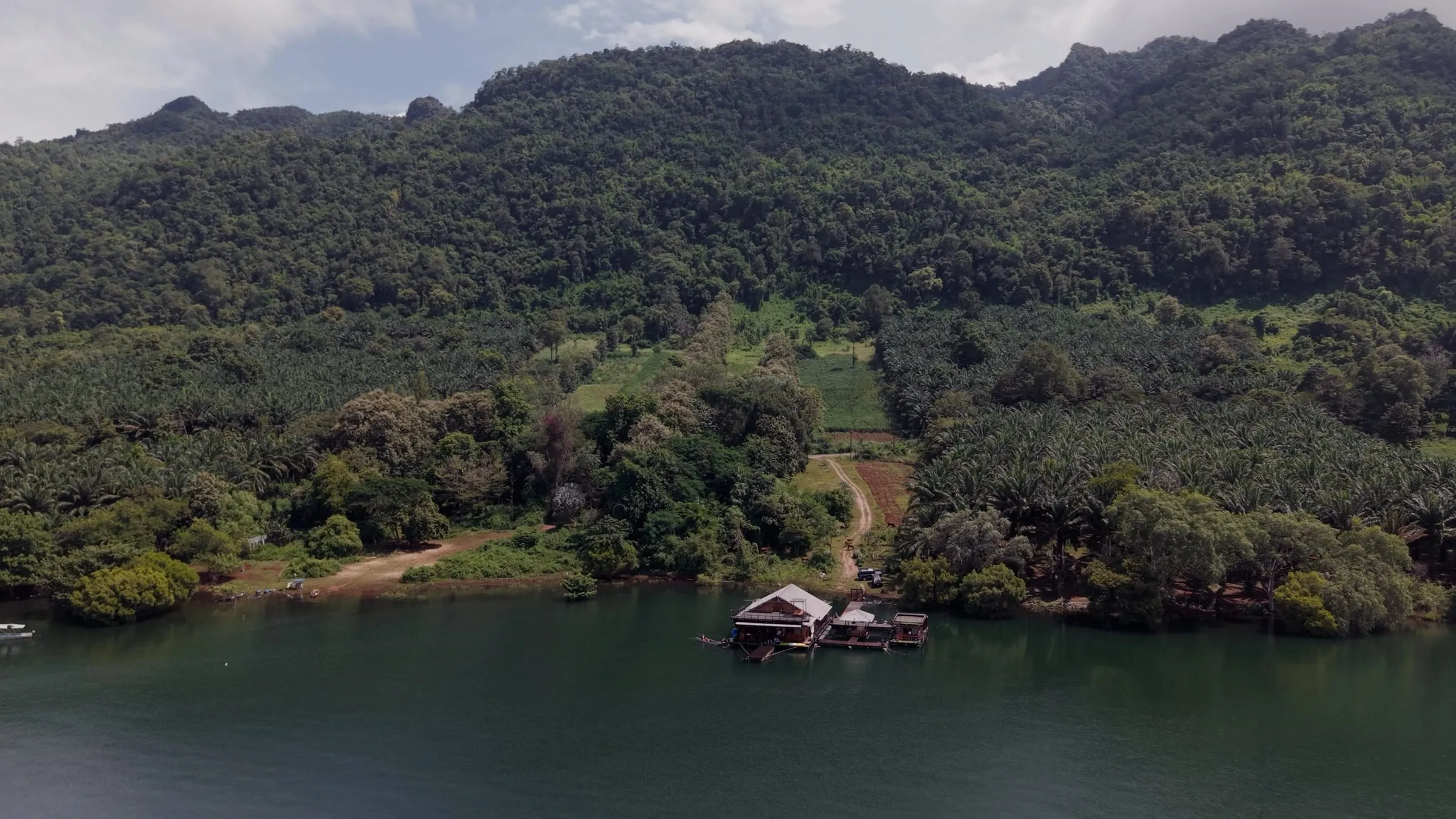 Aerial view of a small floating house tucked against a forested shoreline on the lake.