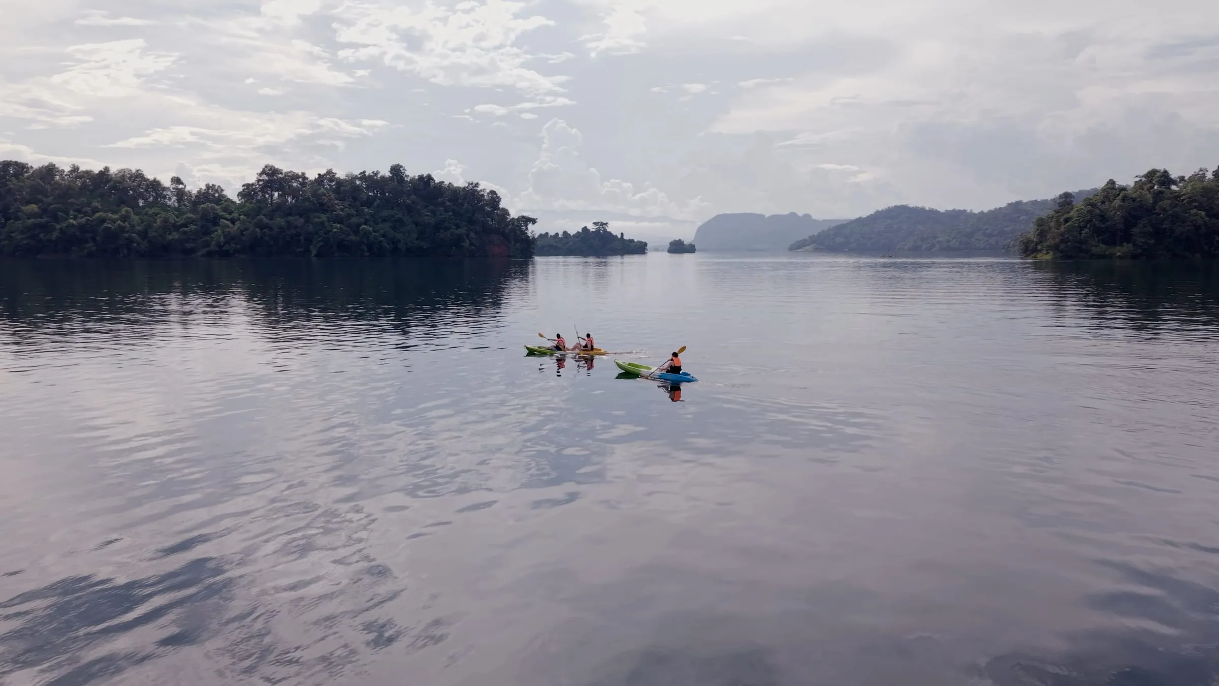 Kayakers paddling across the calm lake between forested hills.