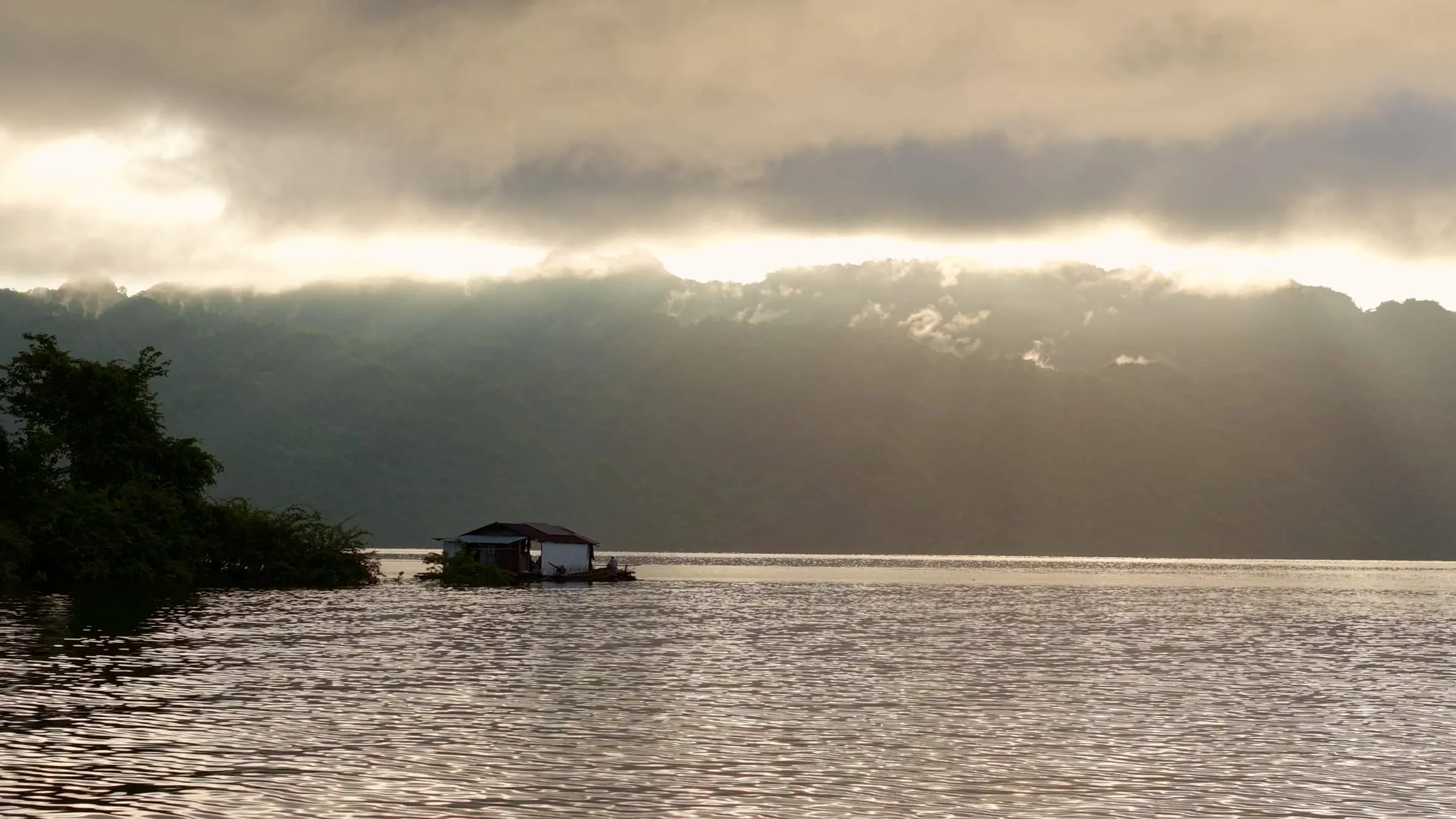 The floating lake house silhouetted under a dramatic golden sky over Khao Laem Lake.