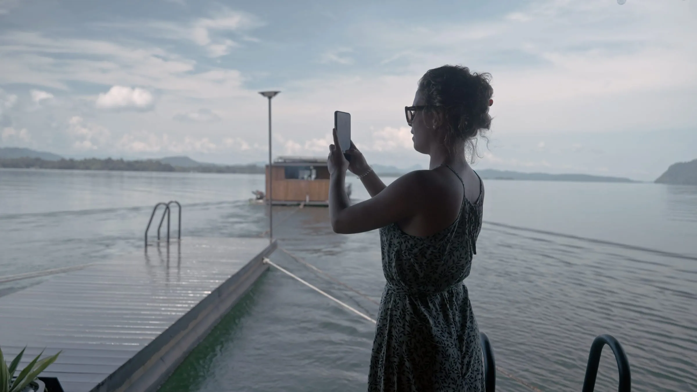 A traveller on the deck of the floating house, photographing the lake at golden hour.