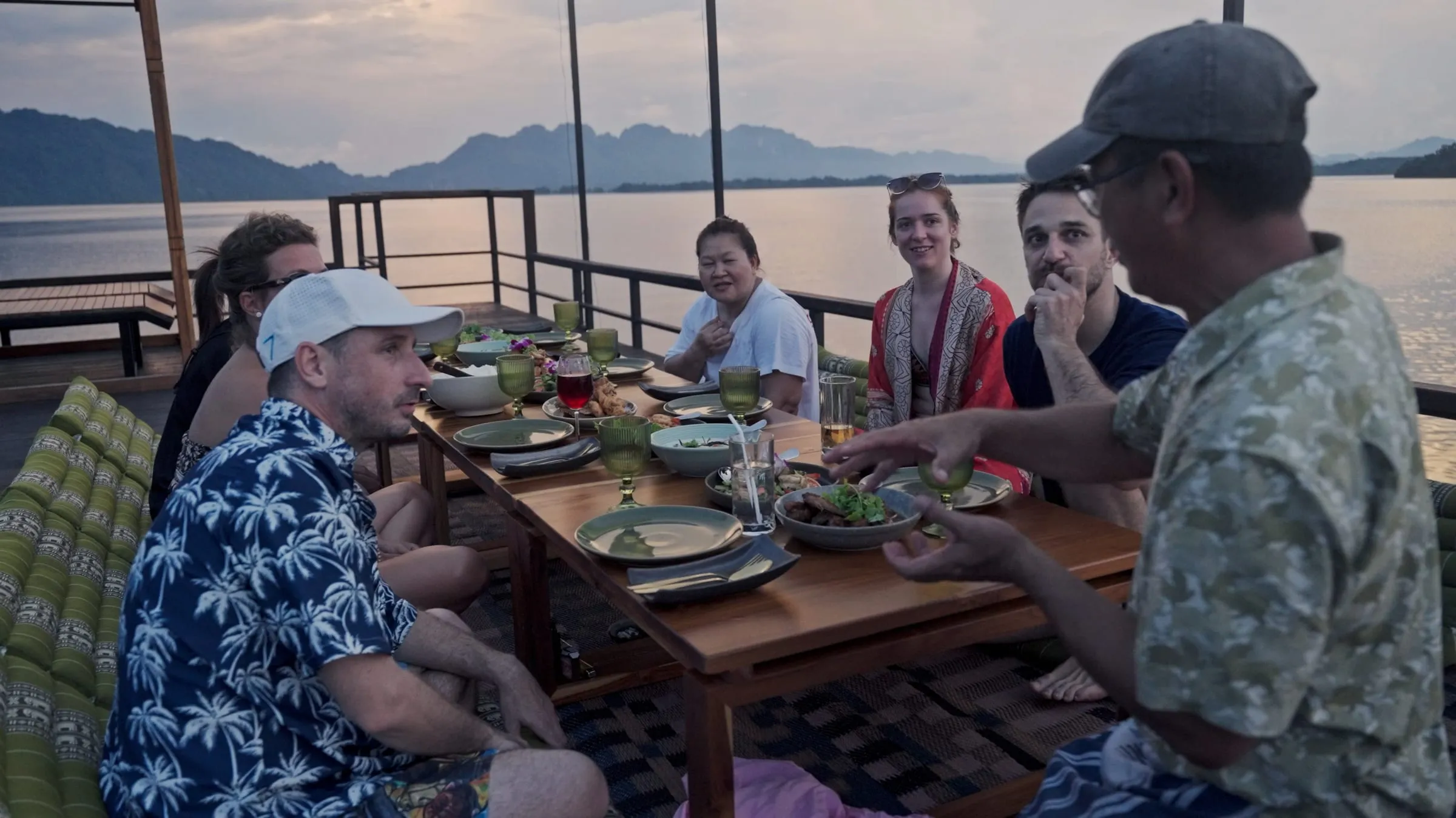 The group gathered on the deck of the floating house, drinks in hand, the lake behind.